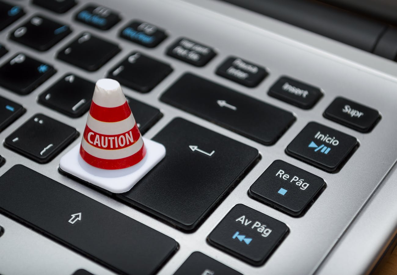 Positive young African American female freelancer in casual clothes talking on smartphone and drinking coffee while working remotely on laptop at home